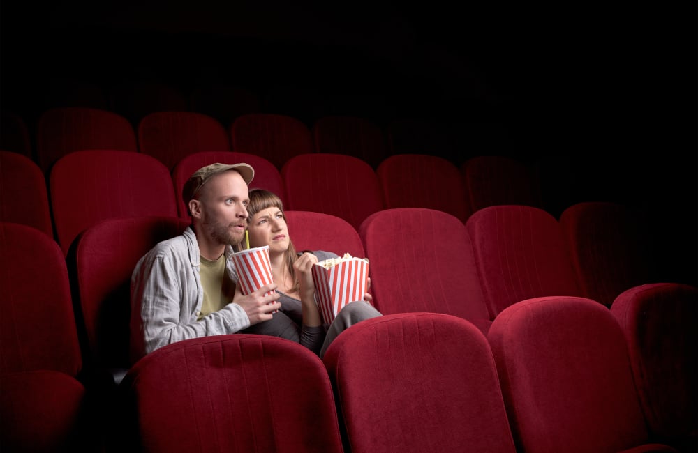 Young cute couple sitting alone at red movie theatre and having fun-1